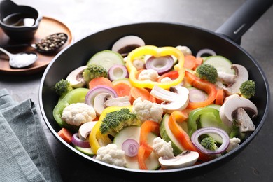 Photo of Frying pan with mix of vegetables, mushrooms and spices on grey table, closeup