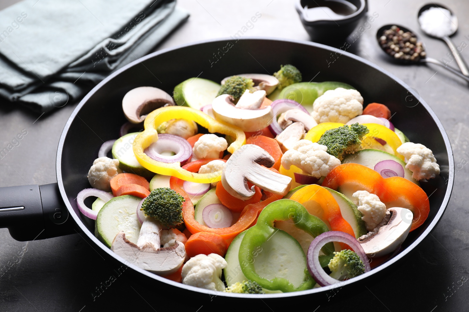 Photo of Frying pan with mix of vegetables, mushrooms and spices on grey table, closeup