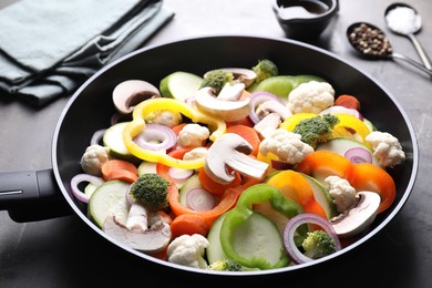 Photo of Frying pan with mix of vegetables, mushrooms and spices on grey table, closeup