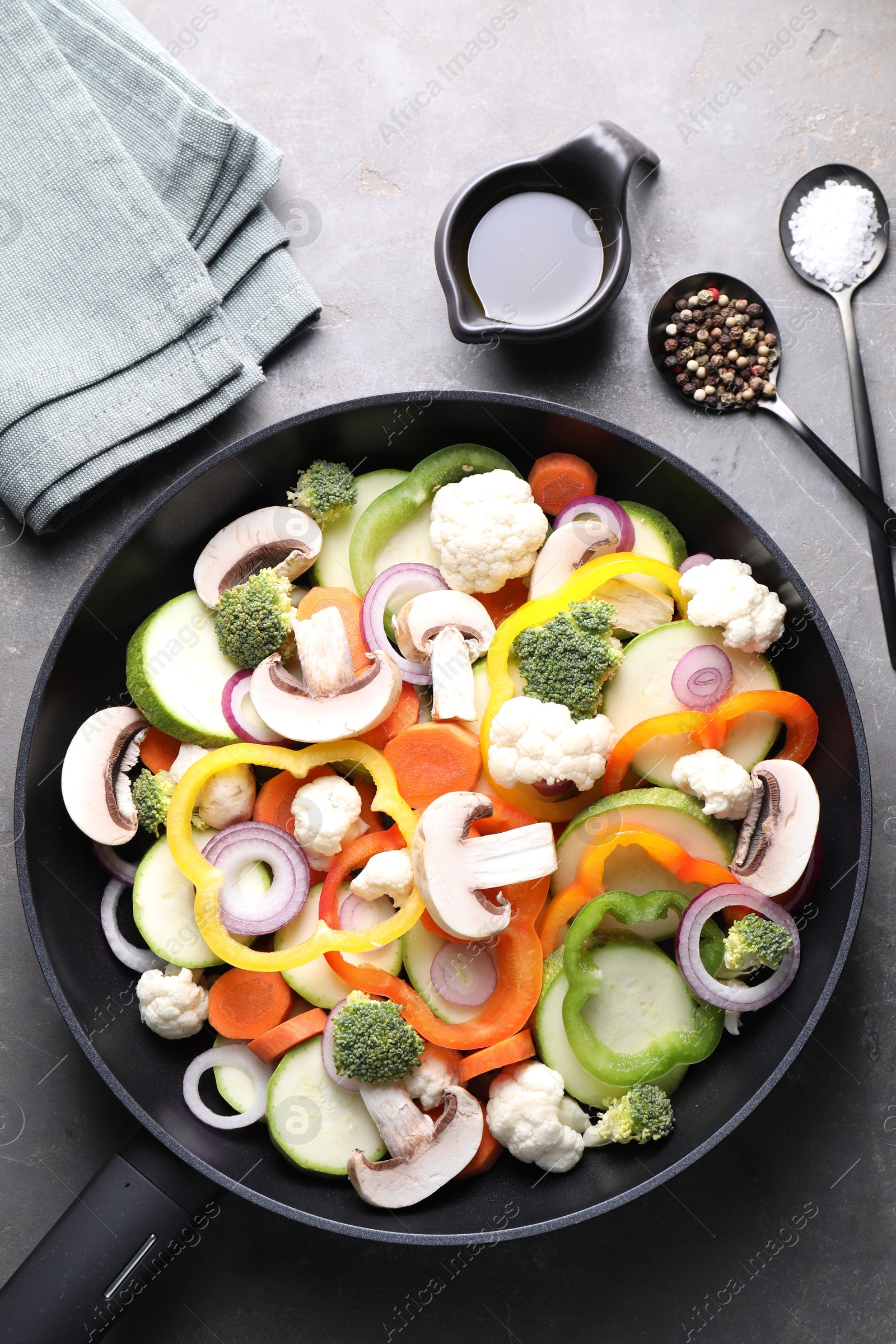 Photo of Frying pan with mix of vegetables, mushrooms and spices on grey table, top view