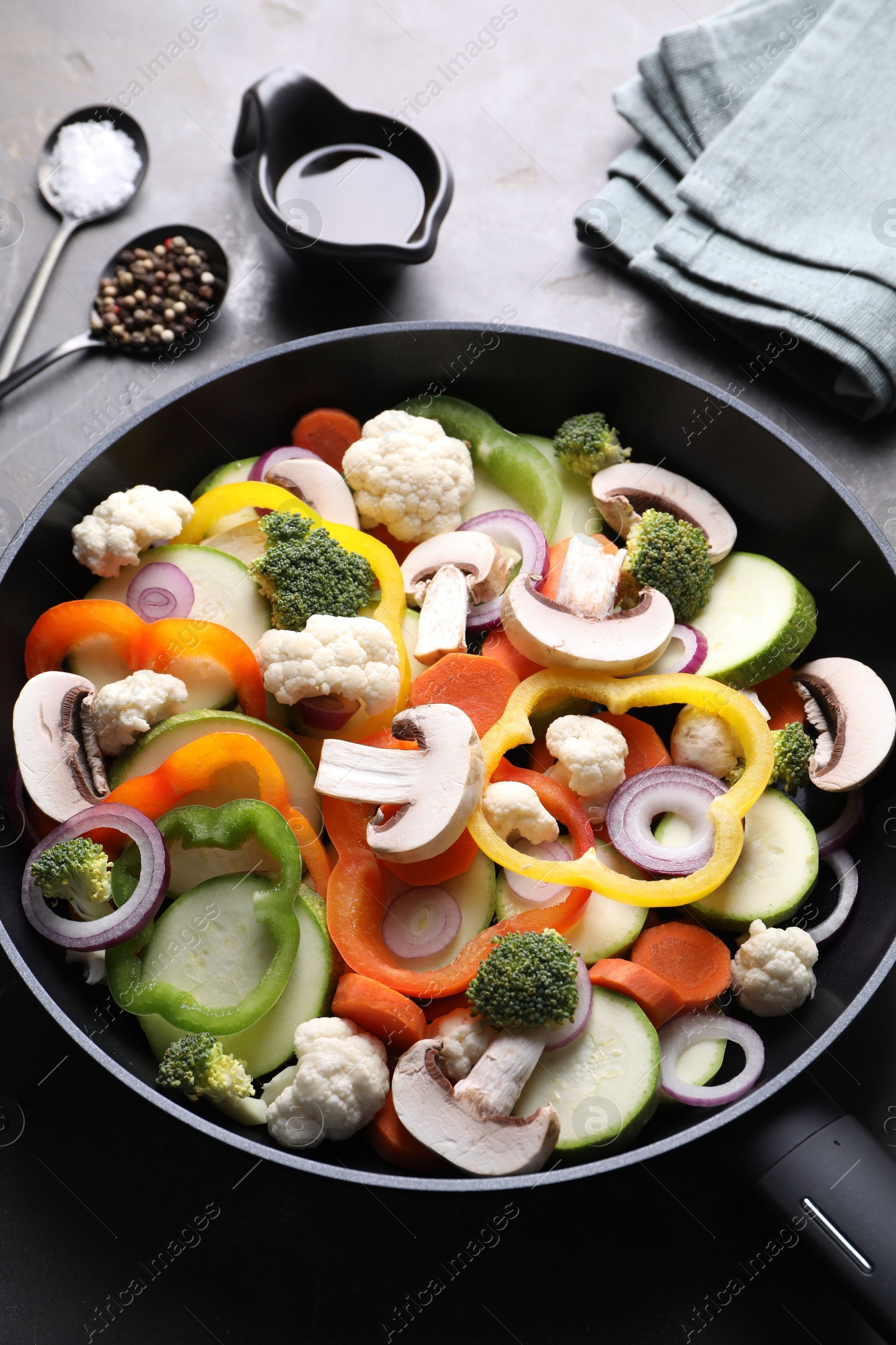 Photo of Frying pan with mix of vegetables, mushrooms and spices on grey table, above view