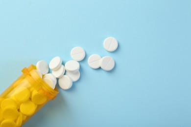 Photo of Bottle of antibiotic pills on light blue background, top view. Space for text