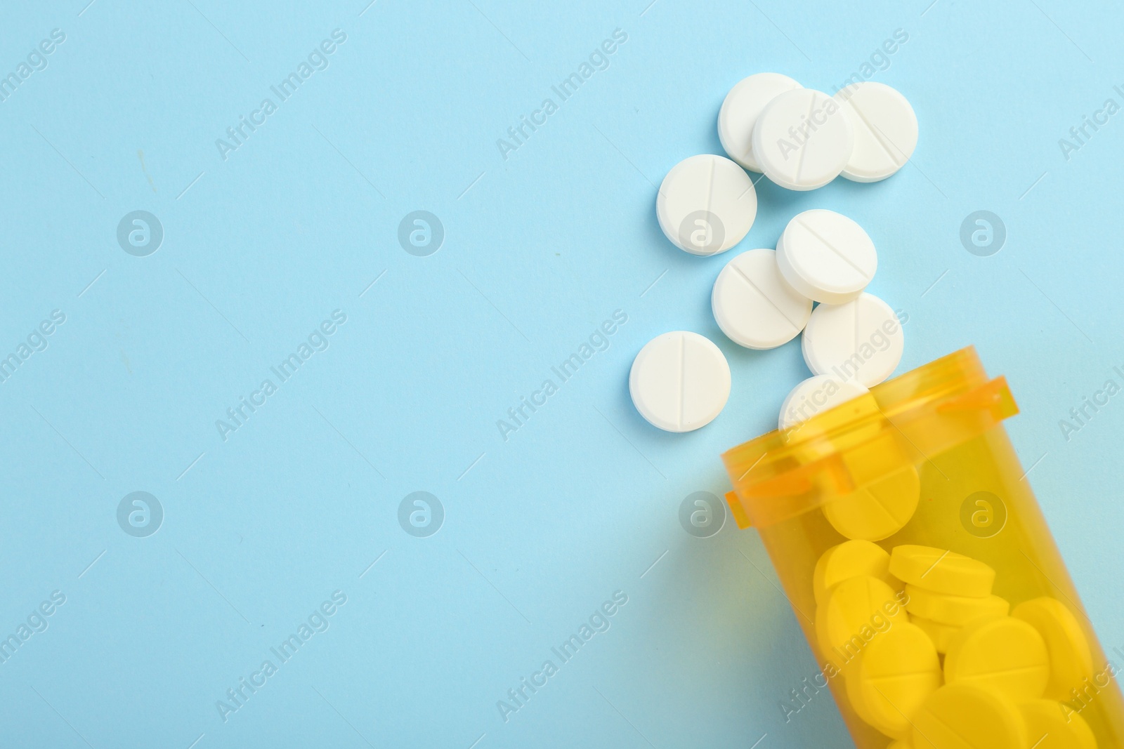 Photo of Bottle of antibiotic pills on light blue background, top view. Space for text