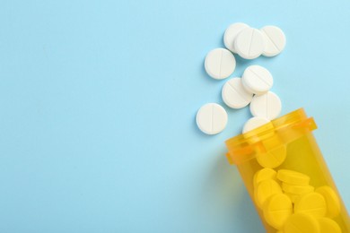 Photo of Bottle of antibiotic pills on light blue background, top view. Space for text