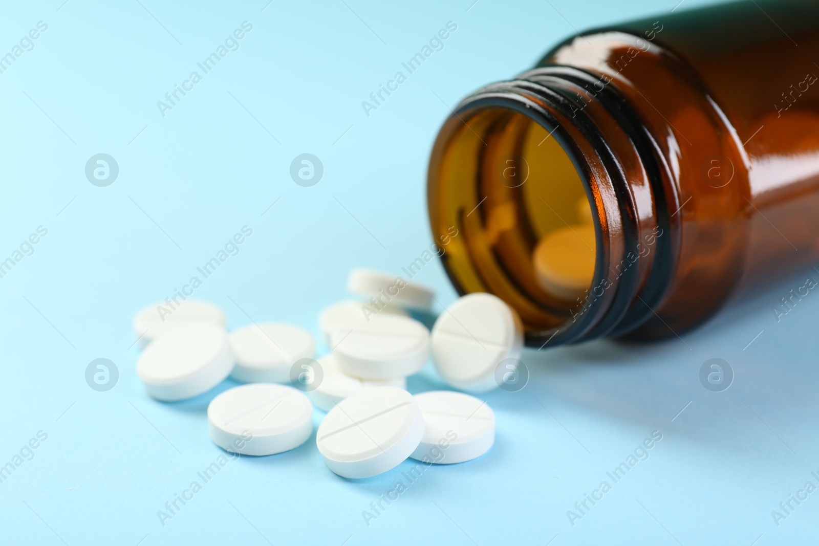 Photo of Bottle of antibiotic pills on light blue background, closeup