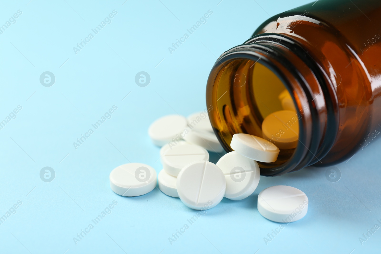 Photo of Bottle of antibiotic pills on light blue background, closeup. Space for text