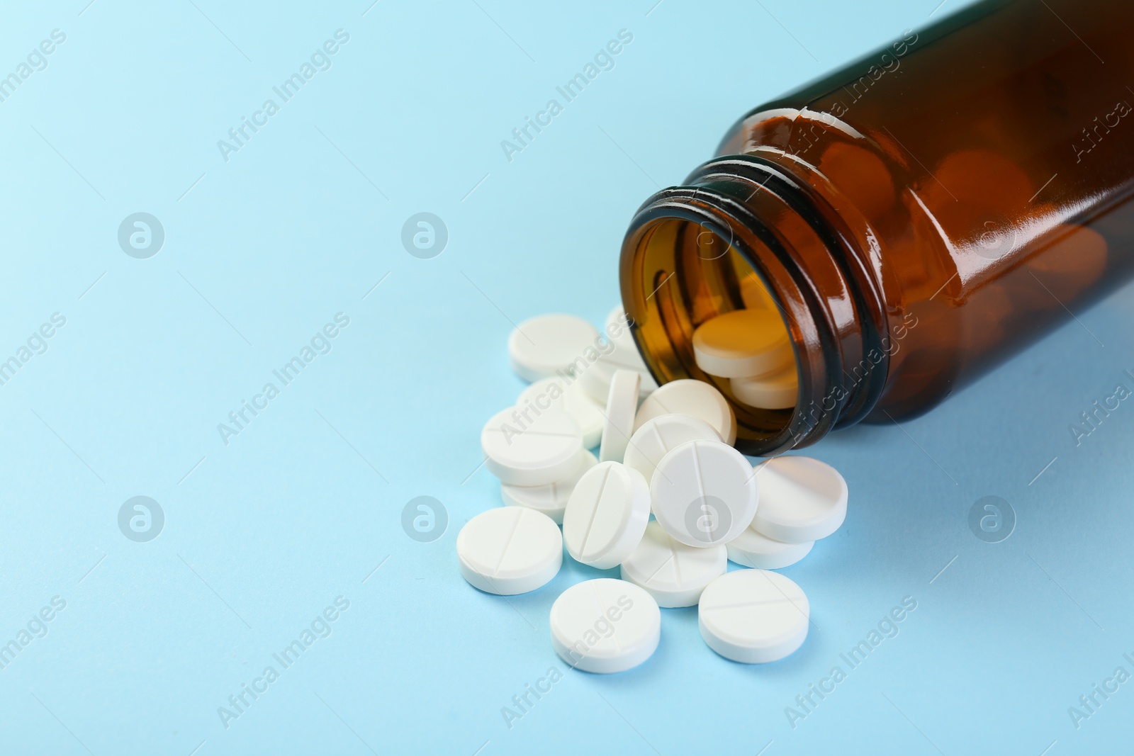 Photo of Bottle of antibiotic pills on light blue background, closeup. Space for text