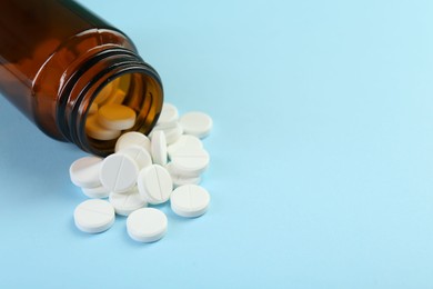 Photo of Bottle of antibiotic pills on light blue background, closeup. Space for text