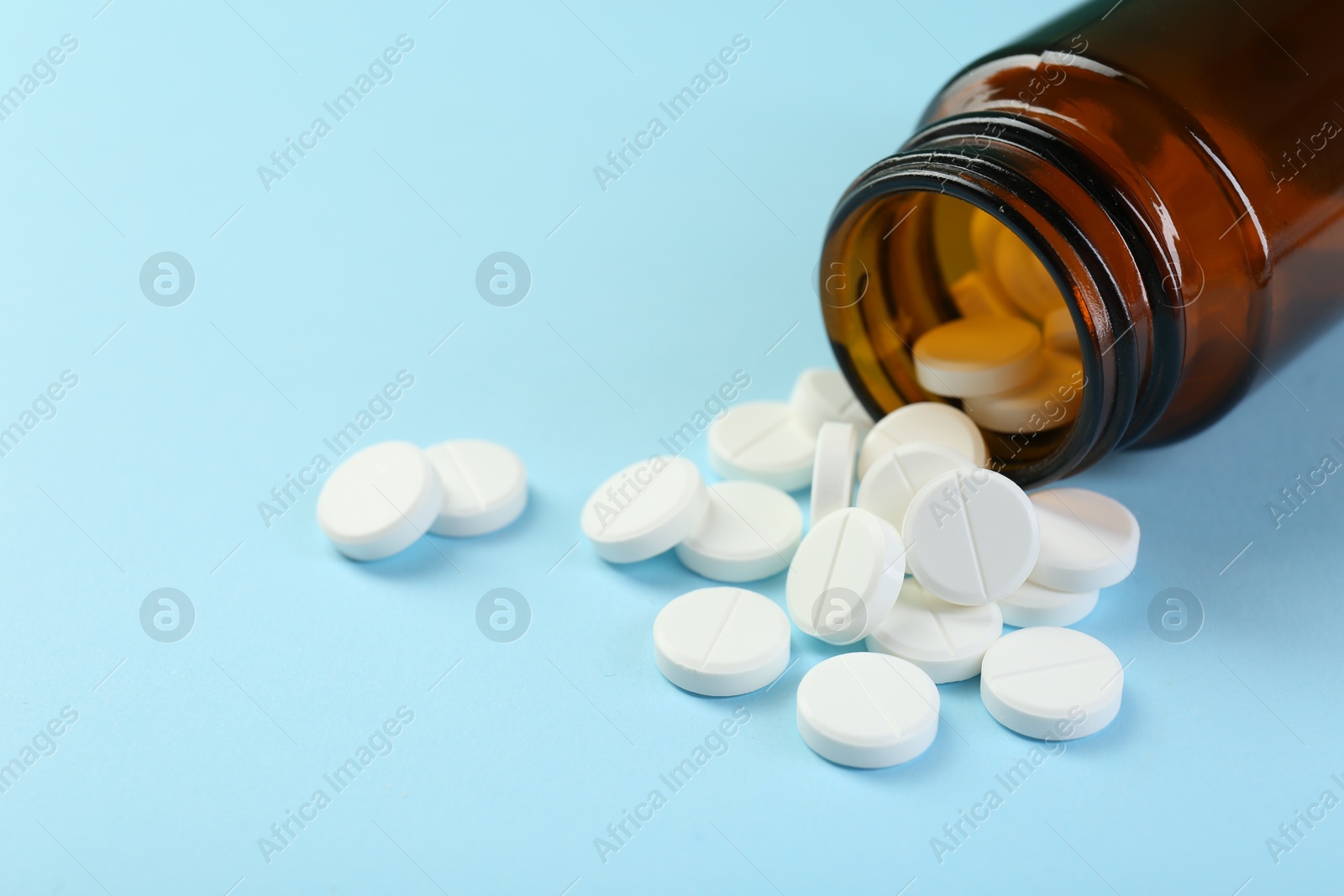 Photo of Bottle of antibiotic pills on light blue background, closeup. Space for text