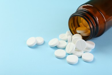 Photo of Bottle of antibiotic pills on light blue background, closeup. Space for text