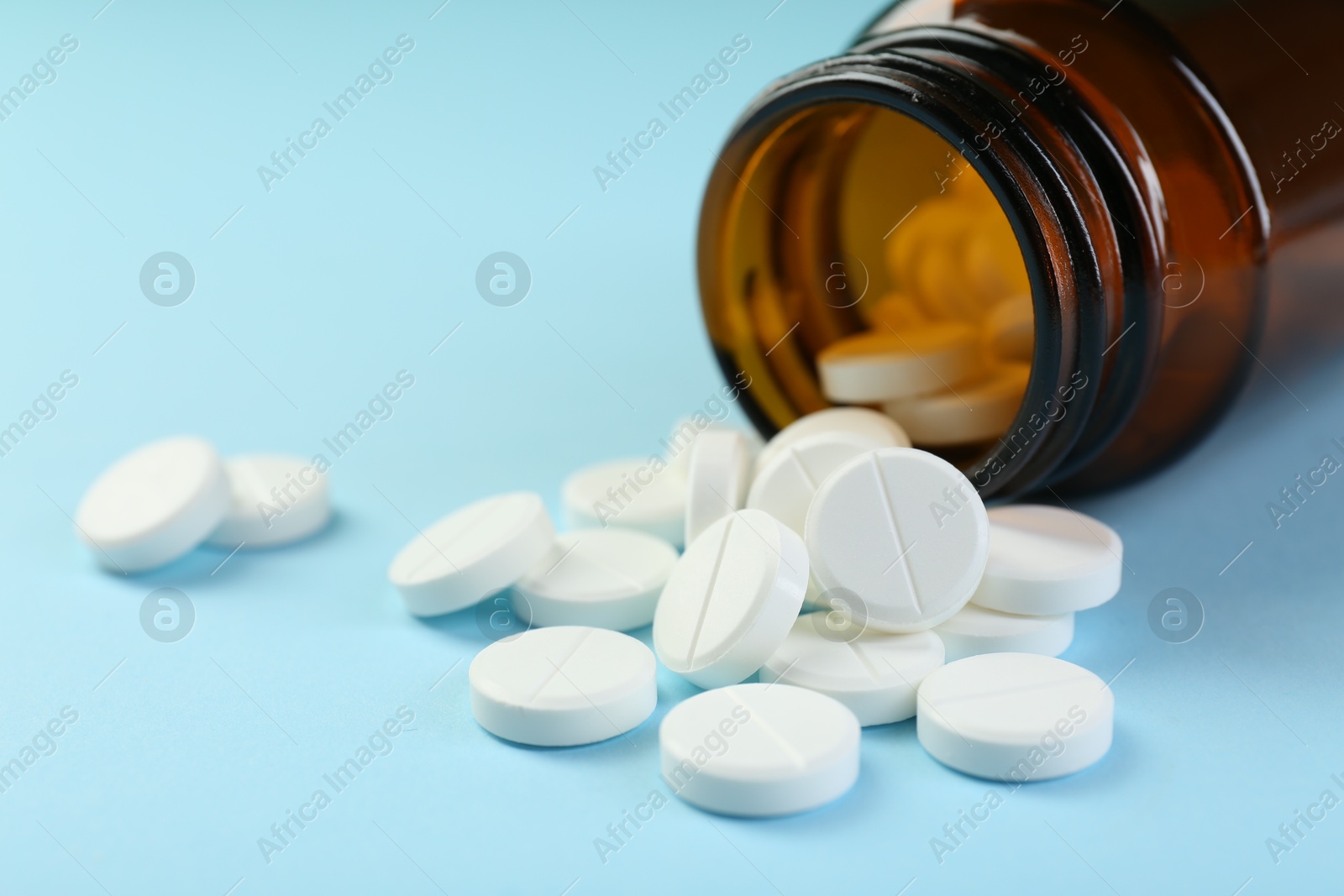 Photo of Bottle of antibiotic pills on light blue background, closeup