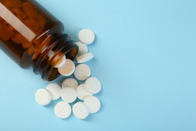 Photo of Bottle of antibiotic pills on light blue background, top view. Space for text