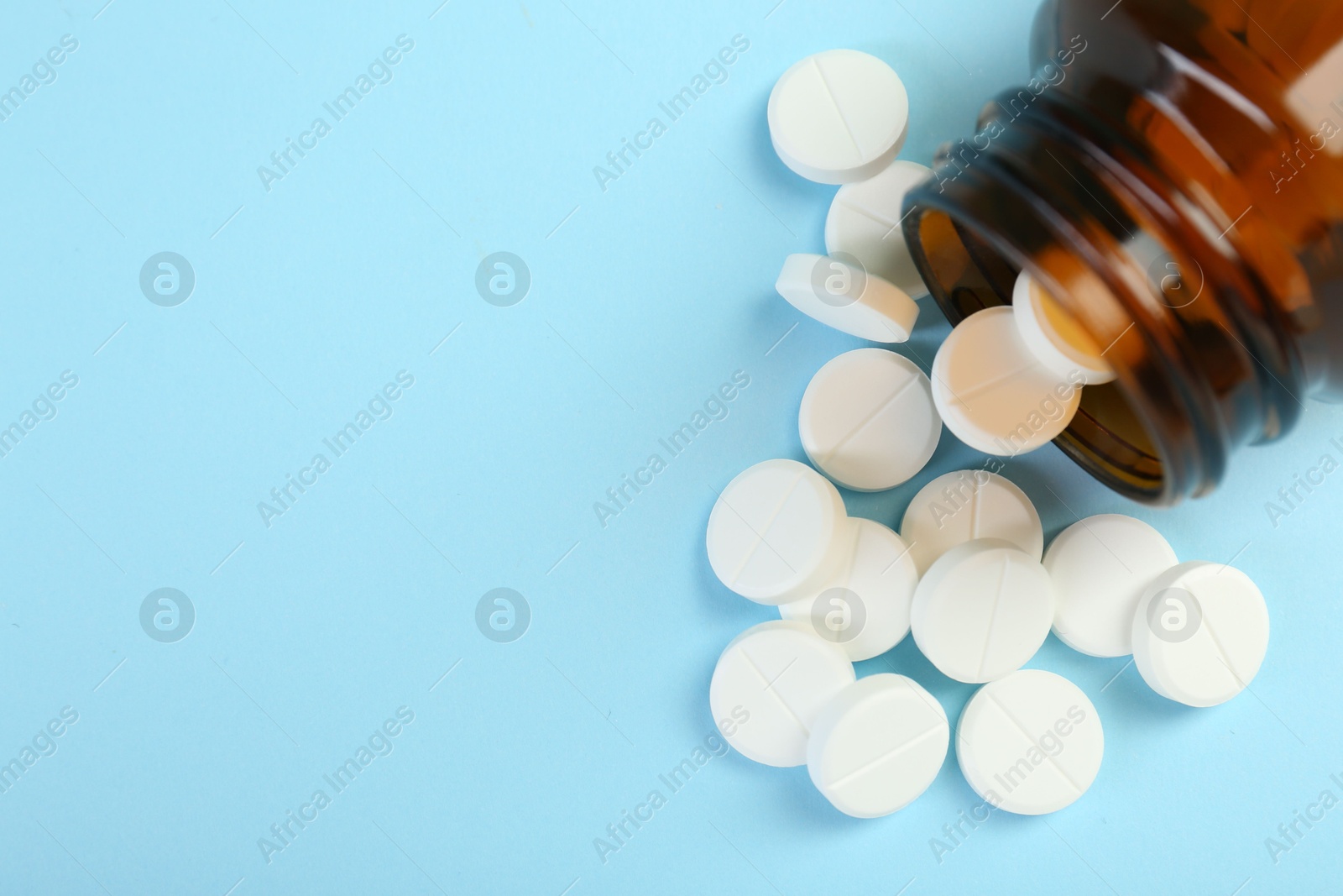 Photo of Bottle of antibiotic pills on light blue background, top view. Space for text