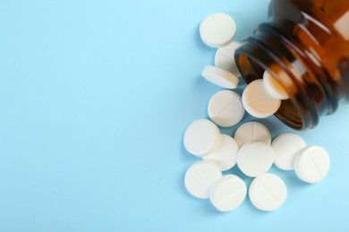 Photo of Bottle of antibiotic pills on light blue background, top view. Space for text