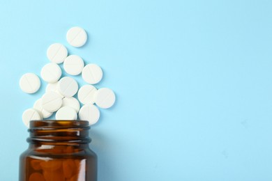 Photo of Bottle of antibiotic pills on light blue background, top view. Space for text