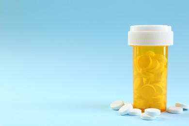 Photo of Bottle of antibiotic pills on light blue background, space for text