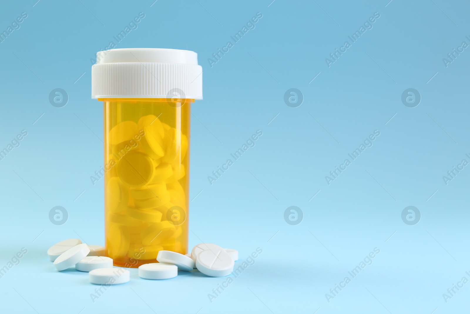 Photo of Bottle of antibiotic pills on light blue background, space for text