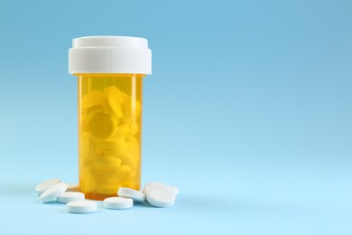 Photo of Bottle of antibiotic pills on light blue background, space for text