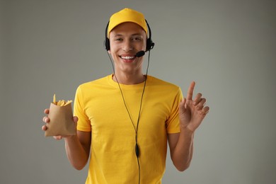 Photo of Fast-food worker with French fries in paper bag on gray background