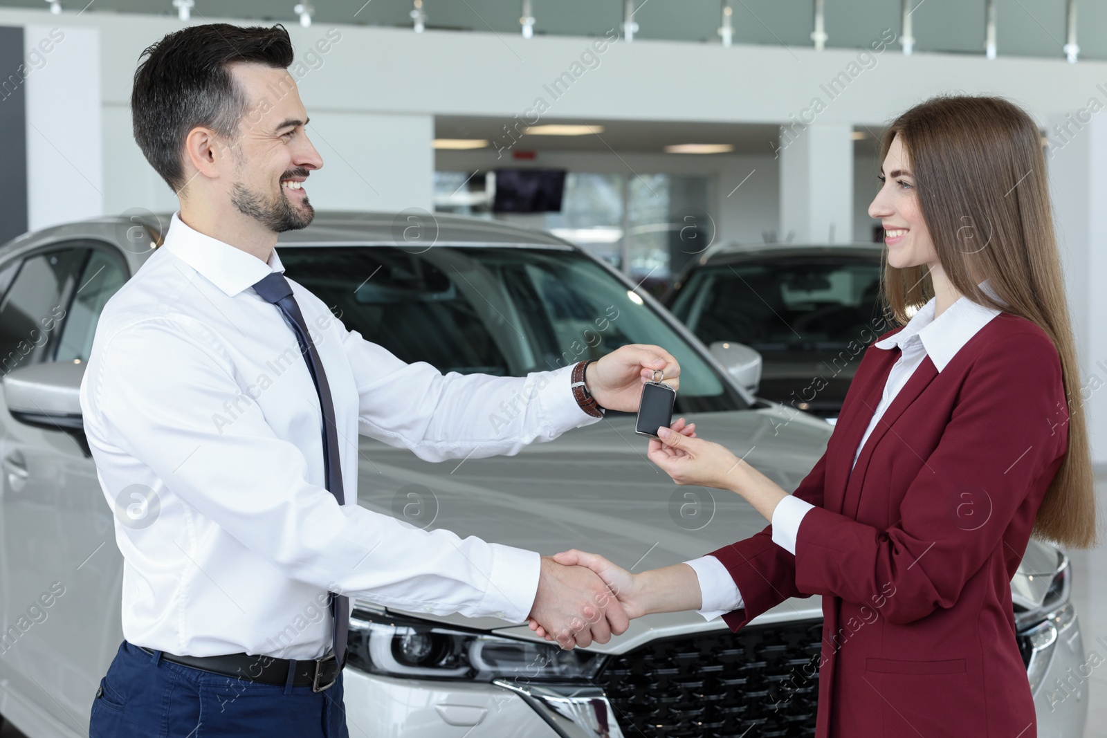 Photo of Salesman giving key to client near new car in salon