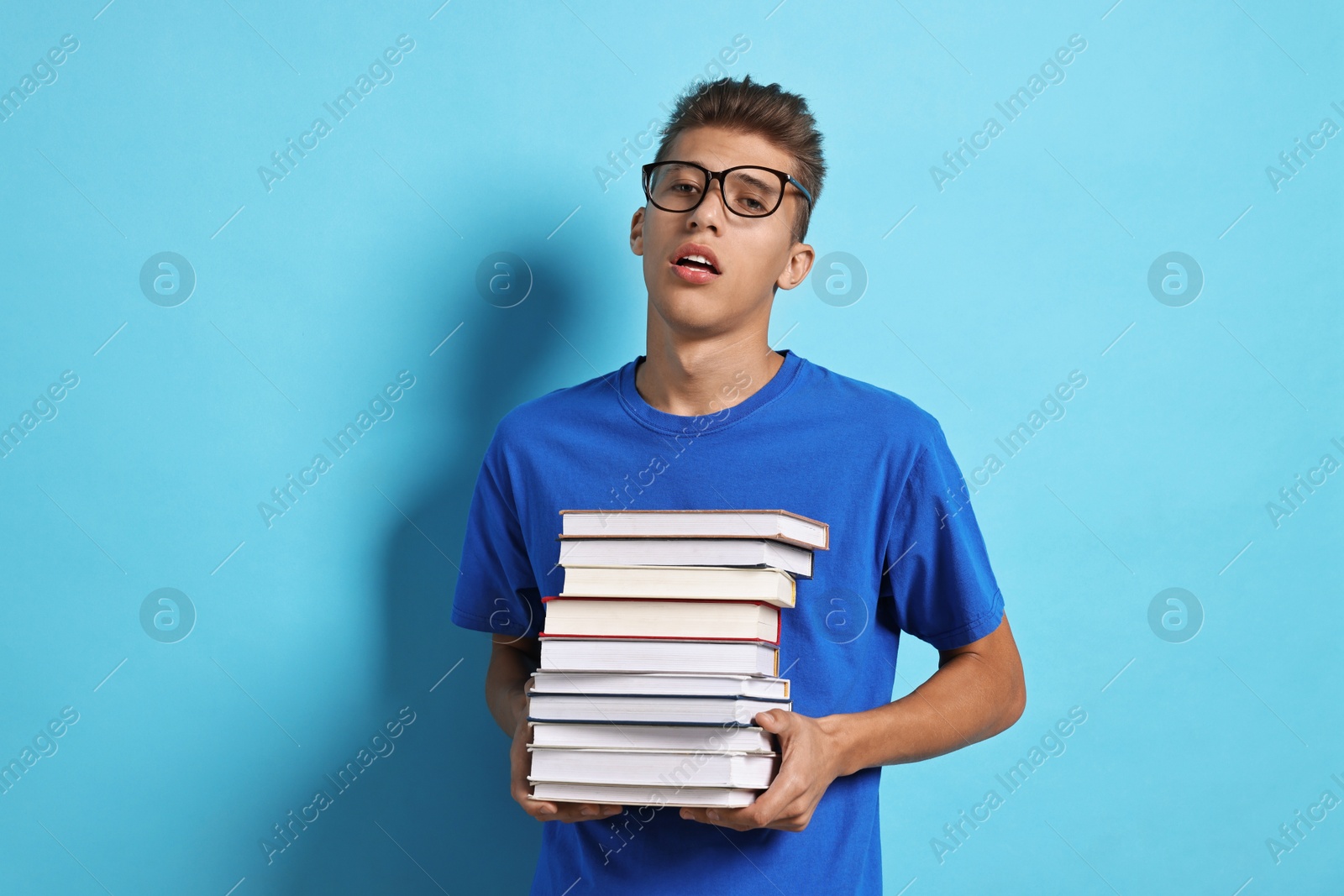 Photo of Tired student with stack of books having stress before exam on light blue background