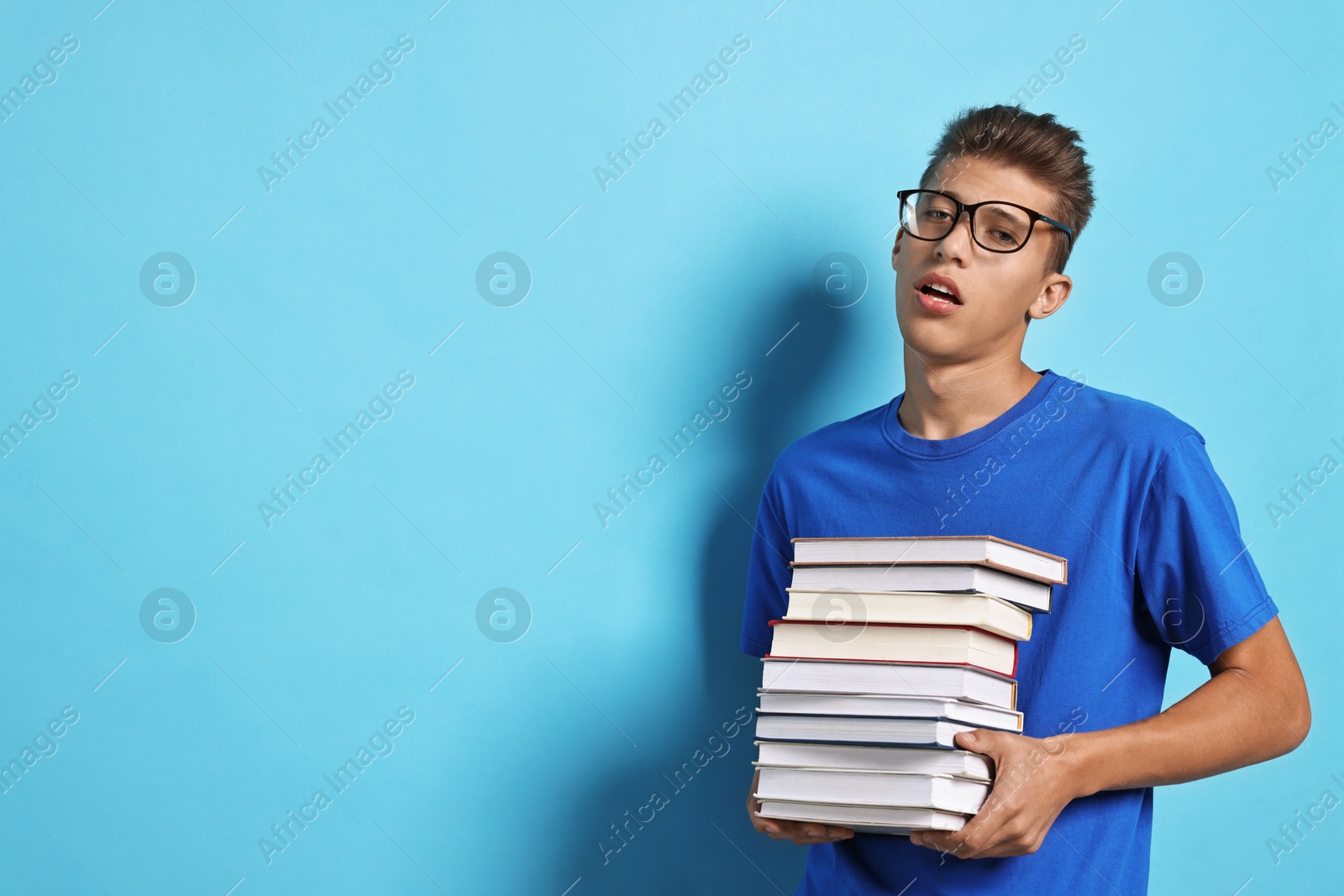 Photo of Tired student with stack of books having stress before exam on light blue background. Space for text