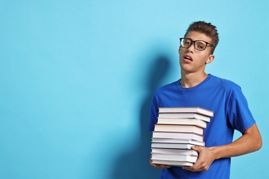 Photo of Tired student with stack of books having stress before exam on light blue background. Space for text