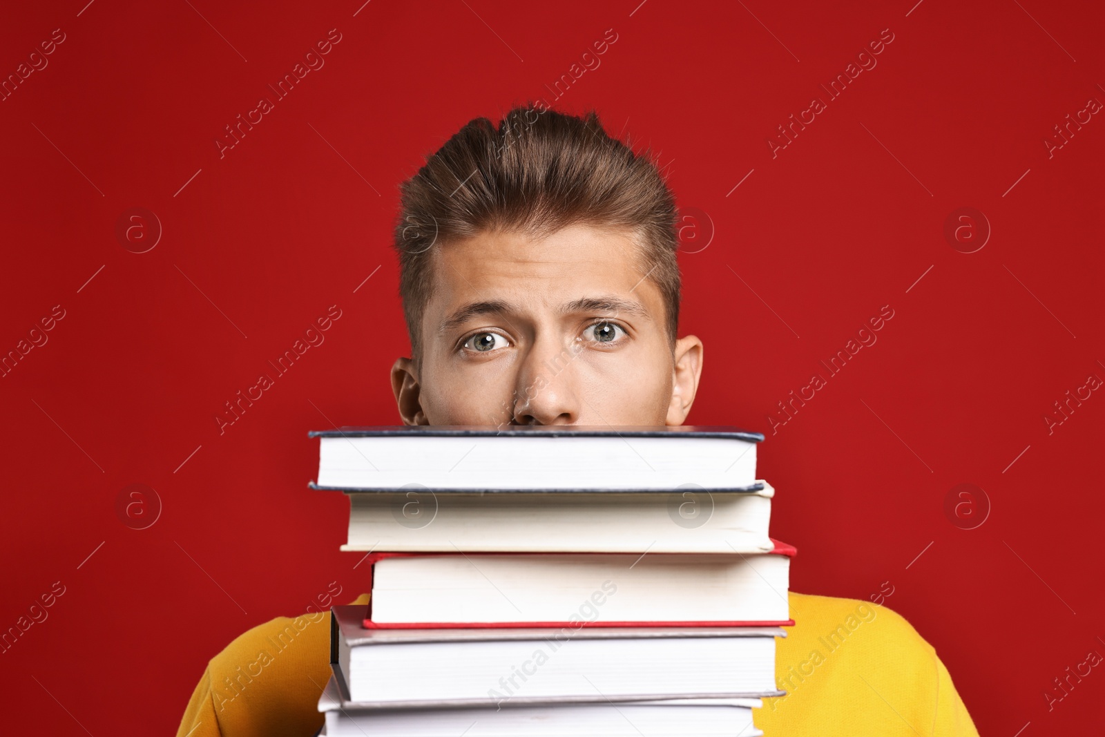 Photo of Emotional student with stack of books having stress before exam on red background