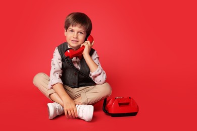 Photo of Cute little boy with old telephone on red background