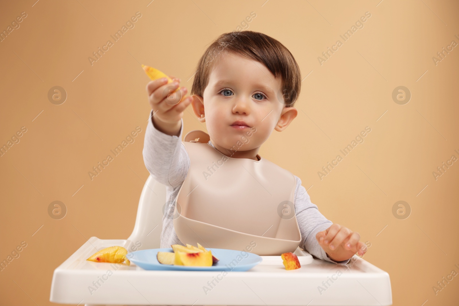 Photo of Healthy baby food. Cute little kid eating fruits in high chair on beige background