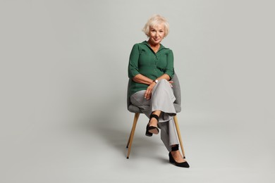 Photo of Beautiful senior woman sitting on chair against light grey background, space for text