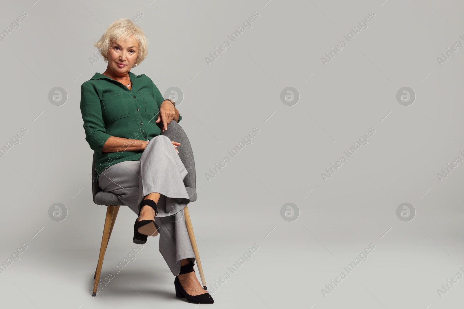 Photo of Beautiful senior woman sitting on chair against light grey background, space for text