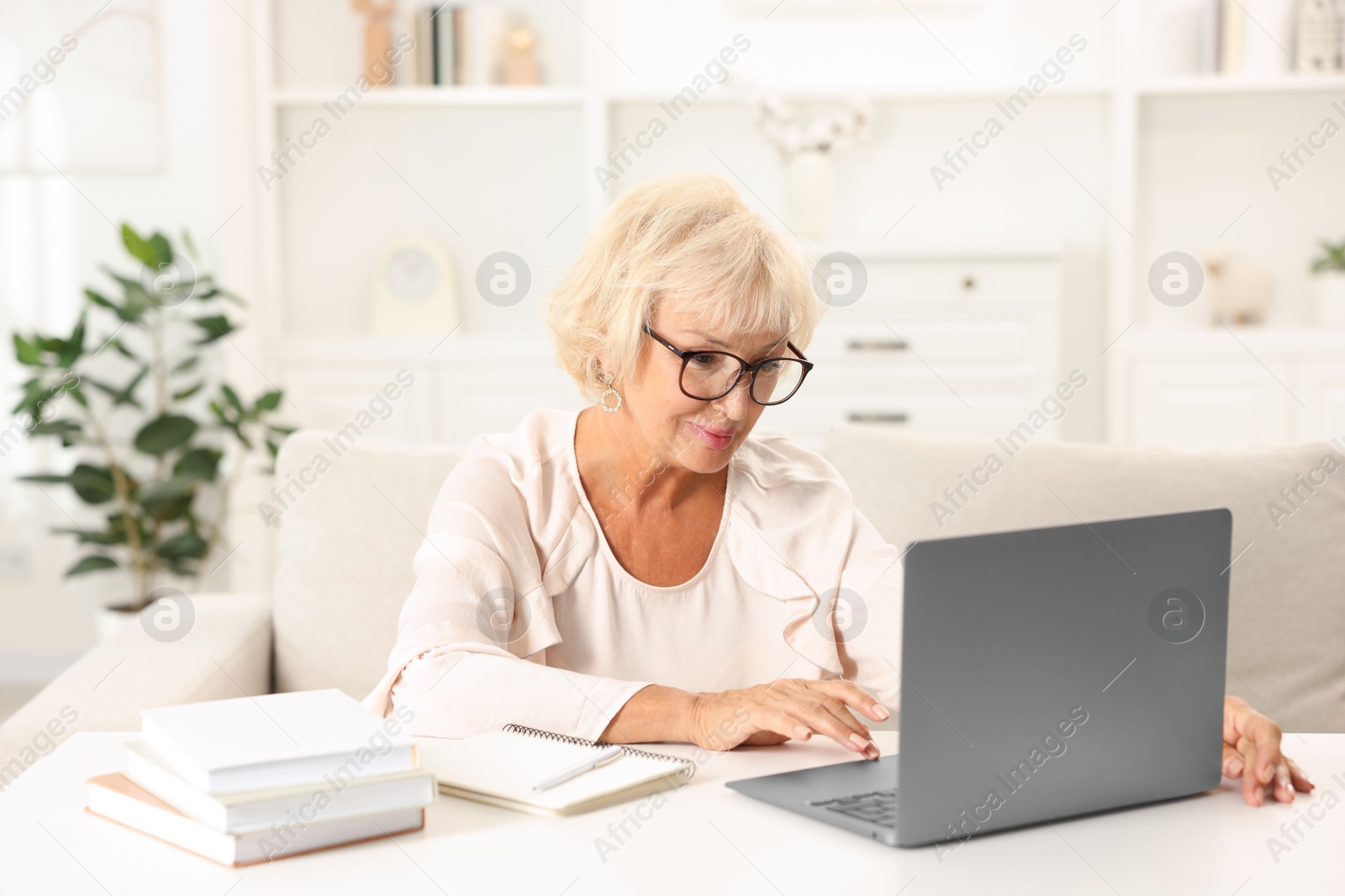 Photo of Beautiful senior woman using laptop at white table indoors