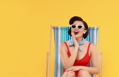 Pin-up woman in swimsuit on folding chair against orange background, space for text