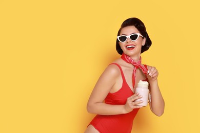 Photo of Pin-up woman in swimsuit with milk shake on orange background, space for text