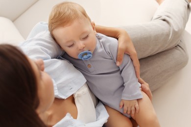 Mother with her sleeping baby on sofa indoors