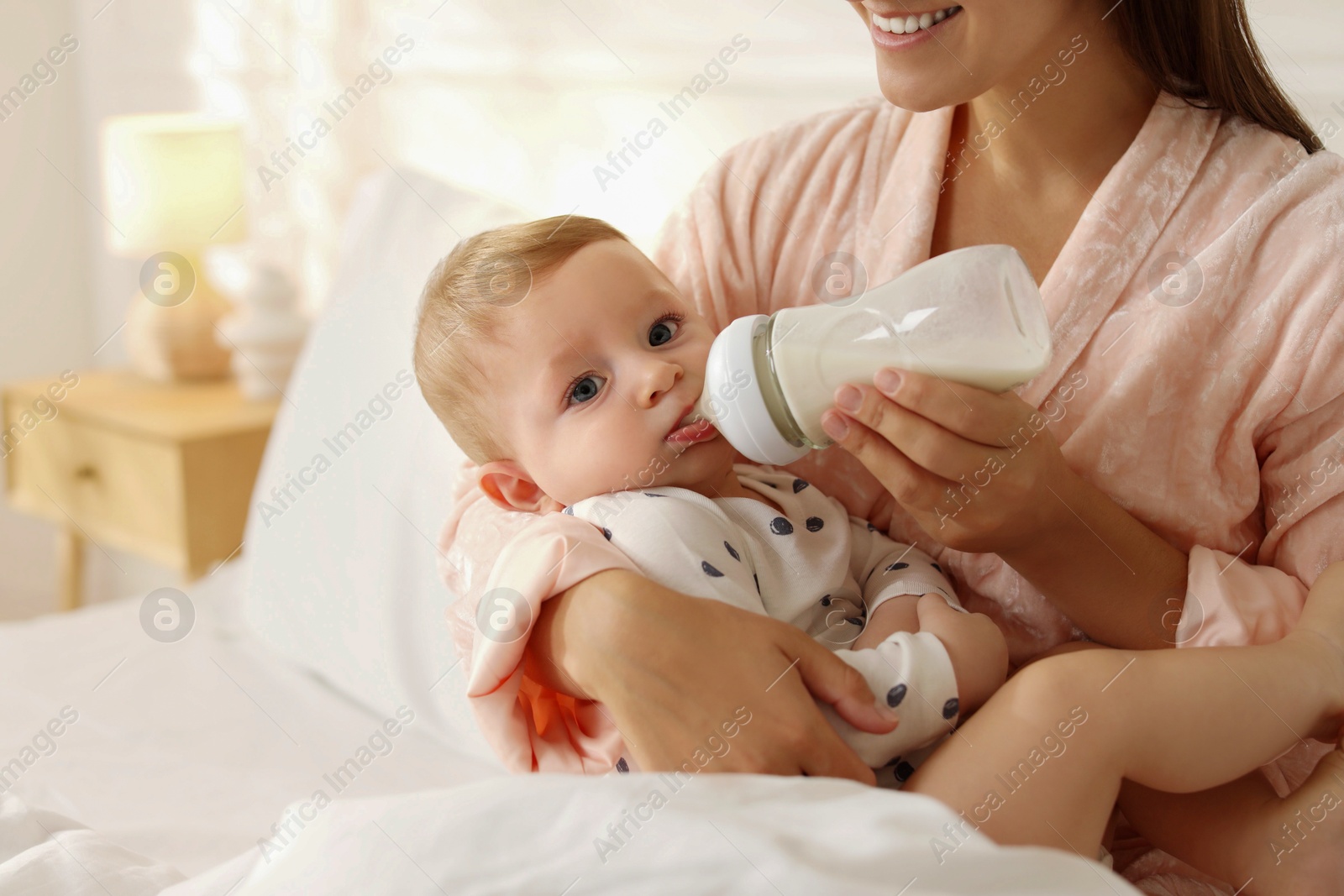 Photo of Mother feeding her little baby from bottle on bed at home, closeup