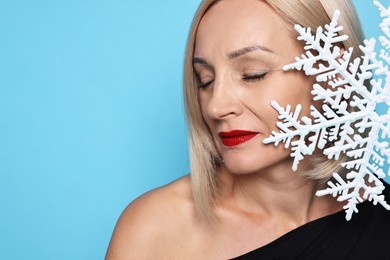 Photo of Woman with decorative snowflake on light blue background, space for text. Christmas celebration