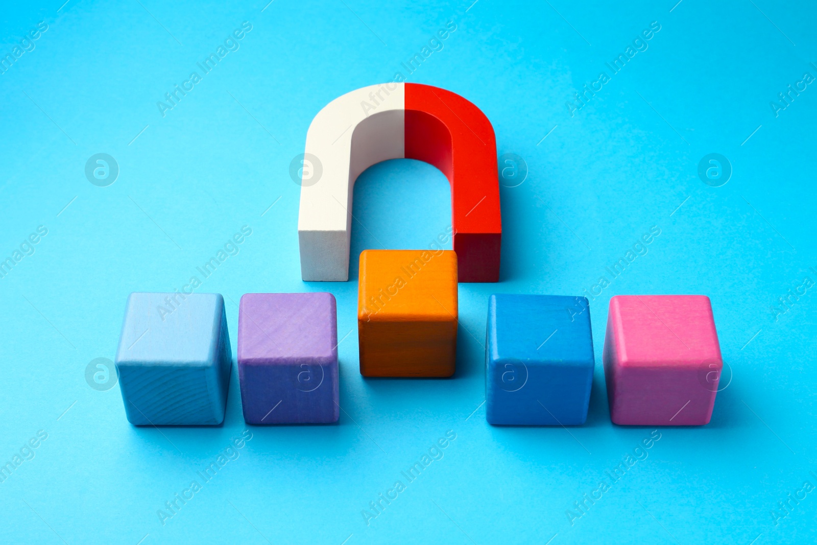 Photo of Magnet attracting colorful cubes on light blue background, closeup