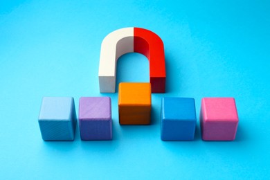 Photo of Magnet attracting colorful cubes on light blue background, closeup