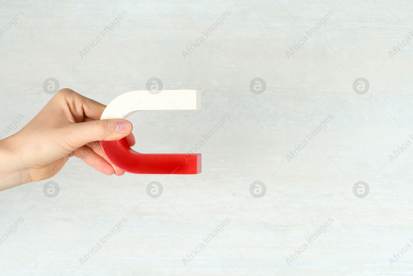 Photo of Woman with horseshoe magnet on light background, closeup. Space for text