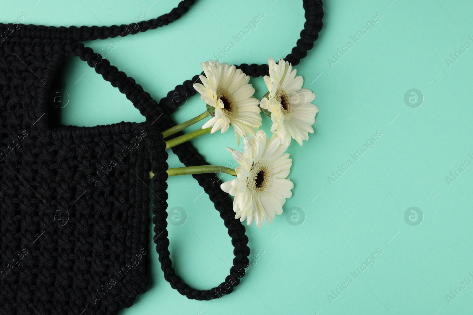 Photo of Macrame shopping bag with beautiful flowers on turquoise background, top view. Space for text