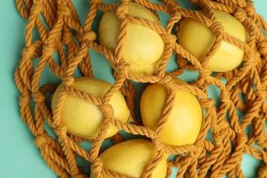 Photo of Macrame shopping bag with lemons on turquoise background, closeup