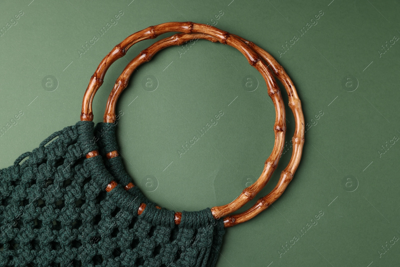 Photo of Macrame shopping bag with wooden handles on green background, top view