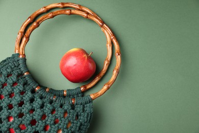 Photo of Macrame shopping bag with wooden handles and apple on green background, flat lay. Space for text