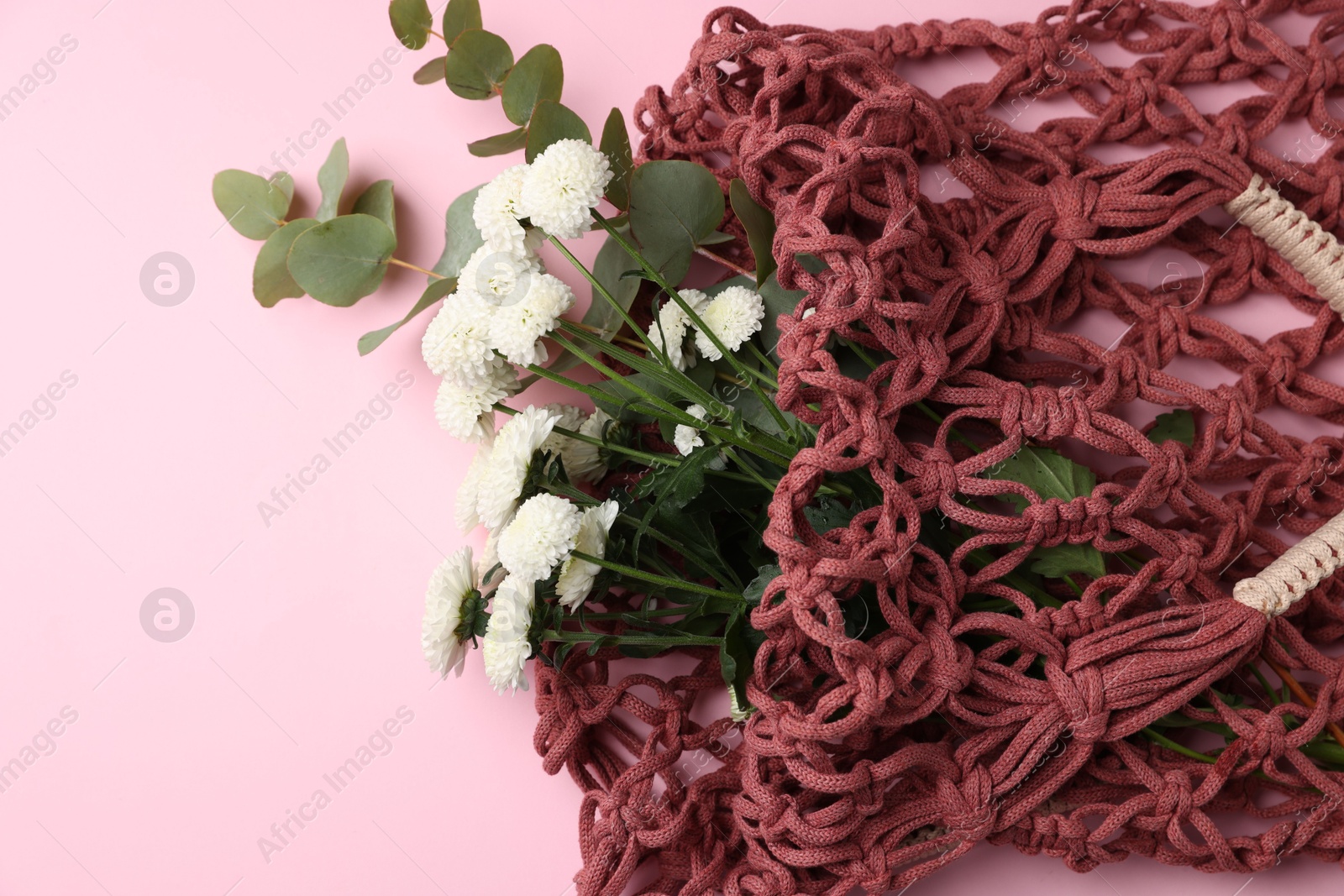 Photo of Macrame shopping bag with flowers and eucalyptus branches on pink background, above view