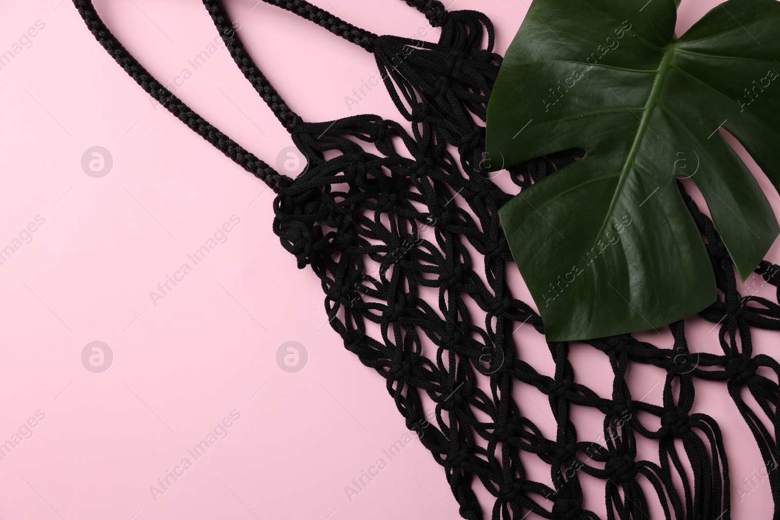 Photo of Macrame shopping bag and monstera leaf on pink background, top view. Space for text