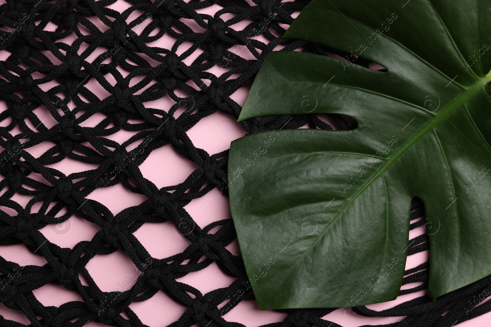 Photo of Macrame shopping bag and monstera leaf on pink background, top view