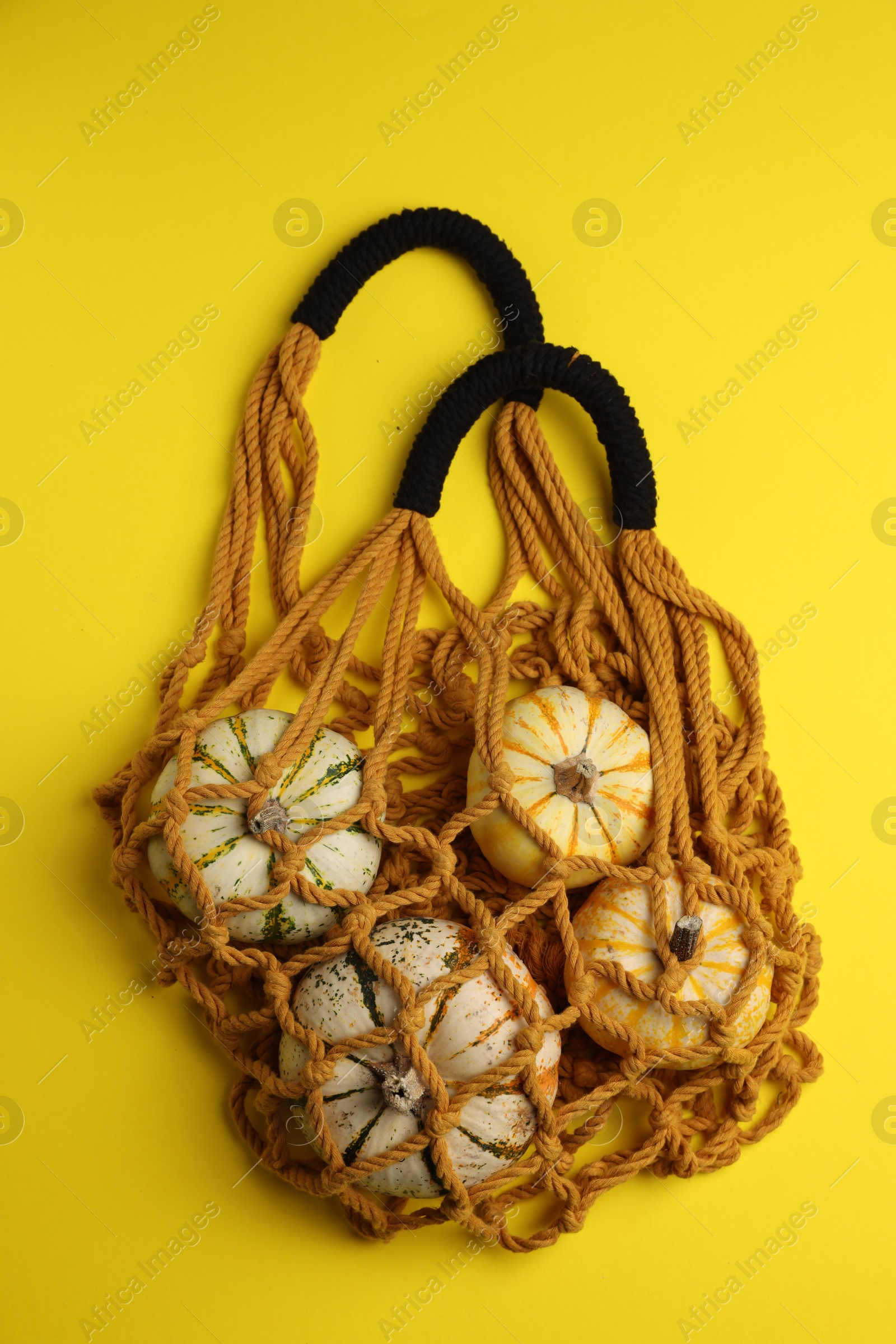 Photo of Macrame shopping bag with pumpkins on yellow background, top view