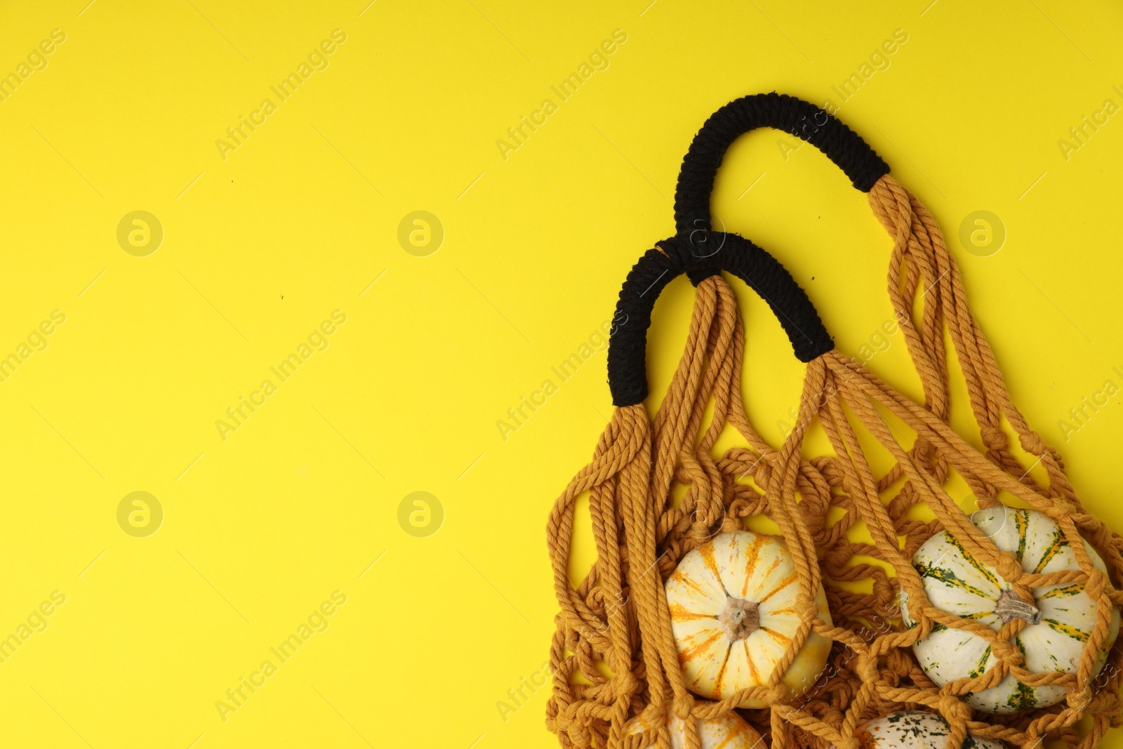 Photo of Macrame shopping bag with pumpkins on yellow background, top view. Space for text